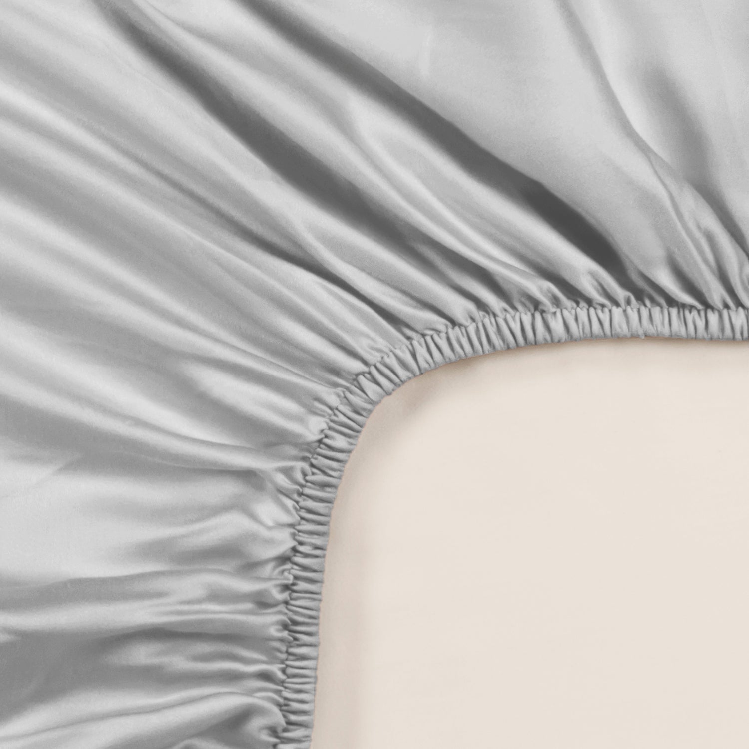 Light grey satin-finish fitted sheet corner with gathered elastic edge and smooth Tencel fabric texture.