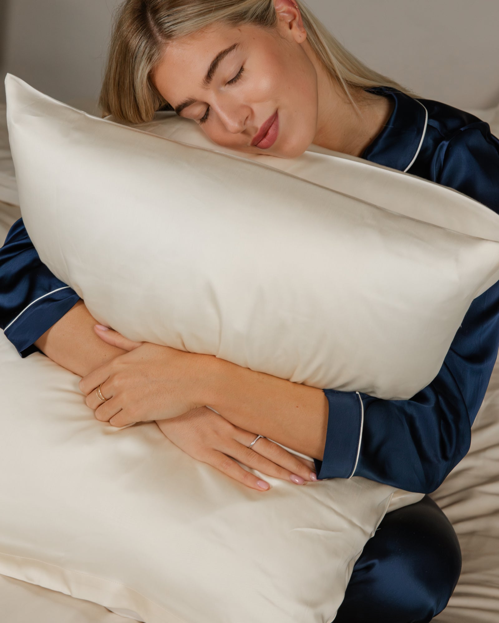 Soft ivory Tencel™ sateen pillowcases with a subtle sheen on a woman in navy satin pajamas.