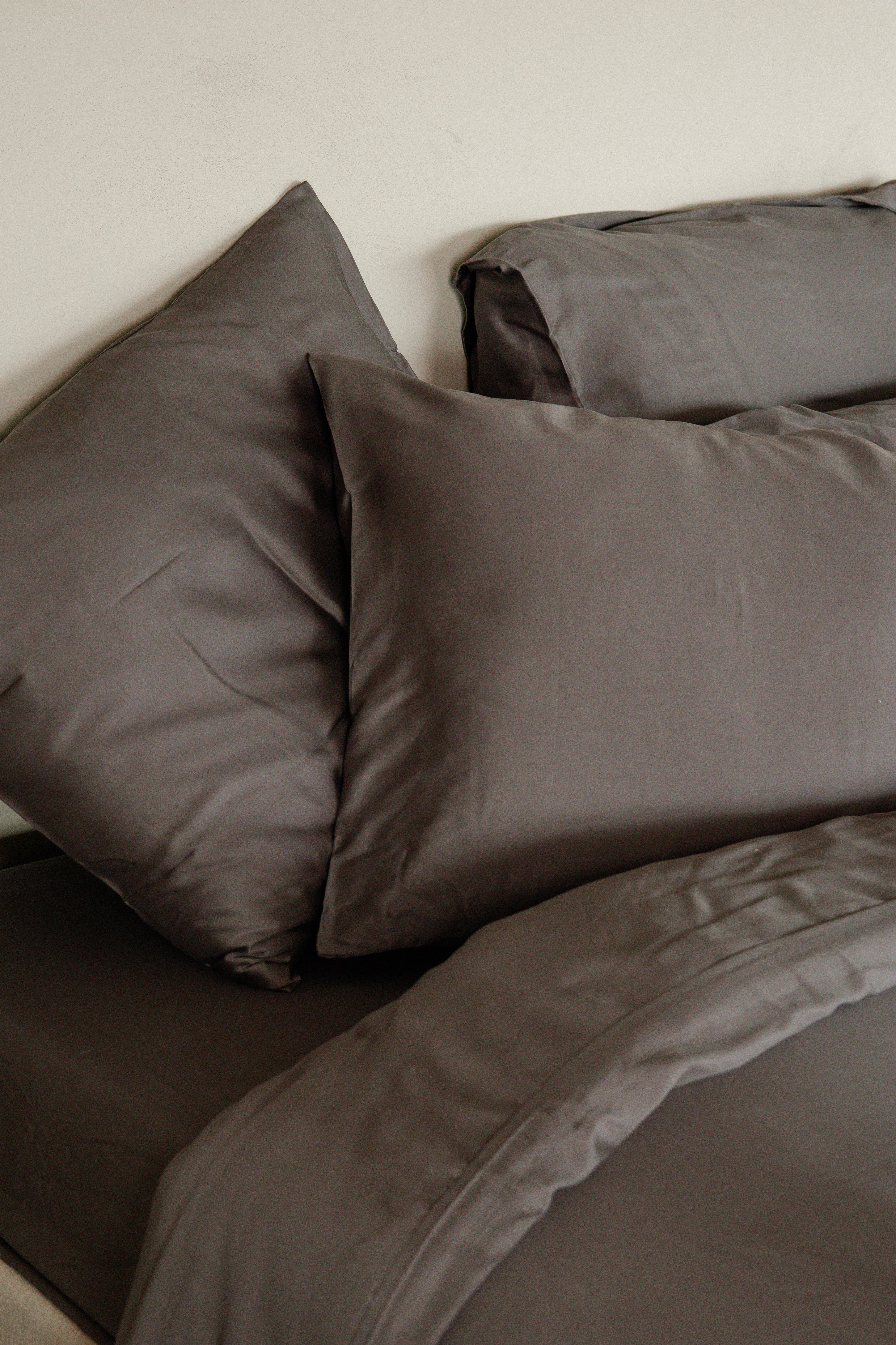 Set of dark grey Tencel™ sateen pillowcases with matching bedsheet and duvet cover.
