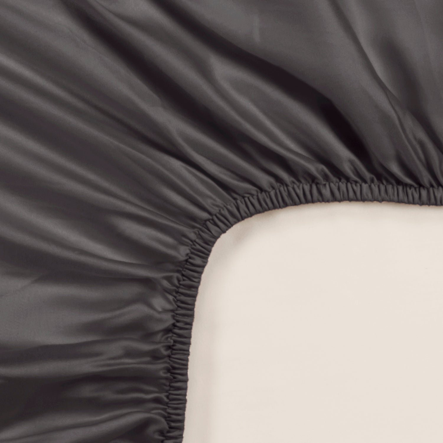 Dark grey Tencel™ sateen fitted sheet corner with smooth, lustrous finish and elastic edge.