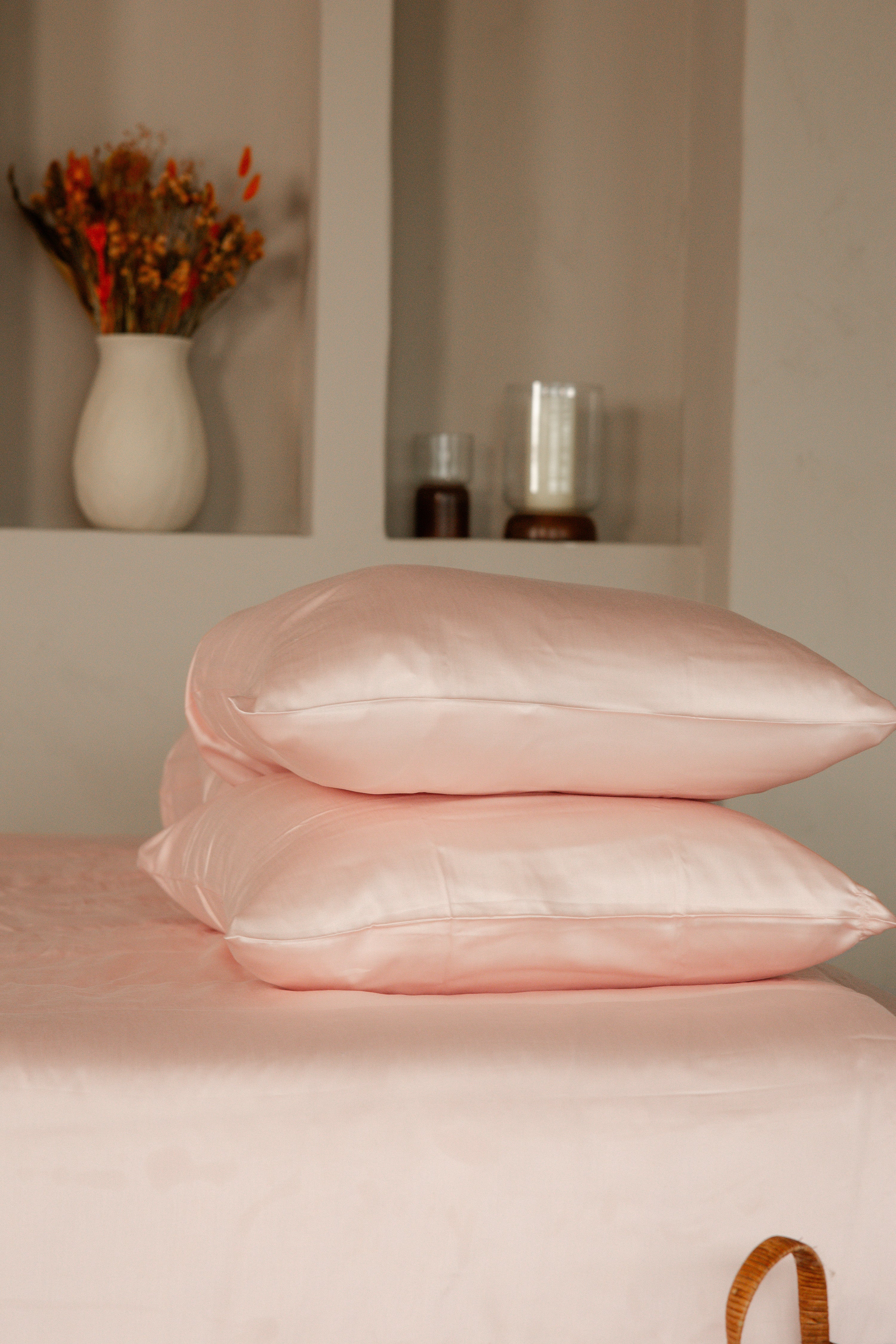 Stack of two soft pink Tencel sateen pillowcases on matching bed linen with a neutral background.