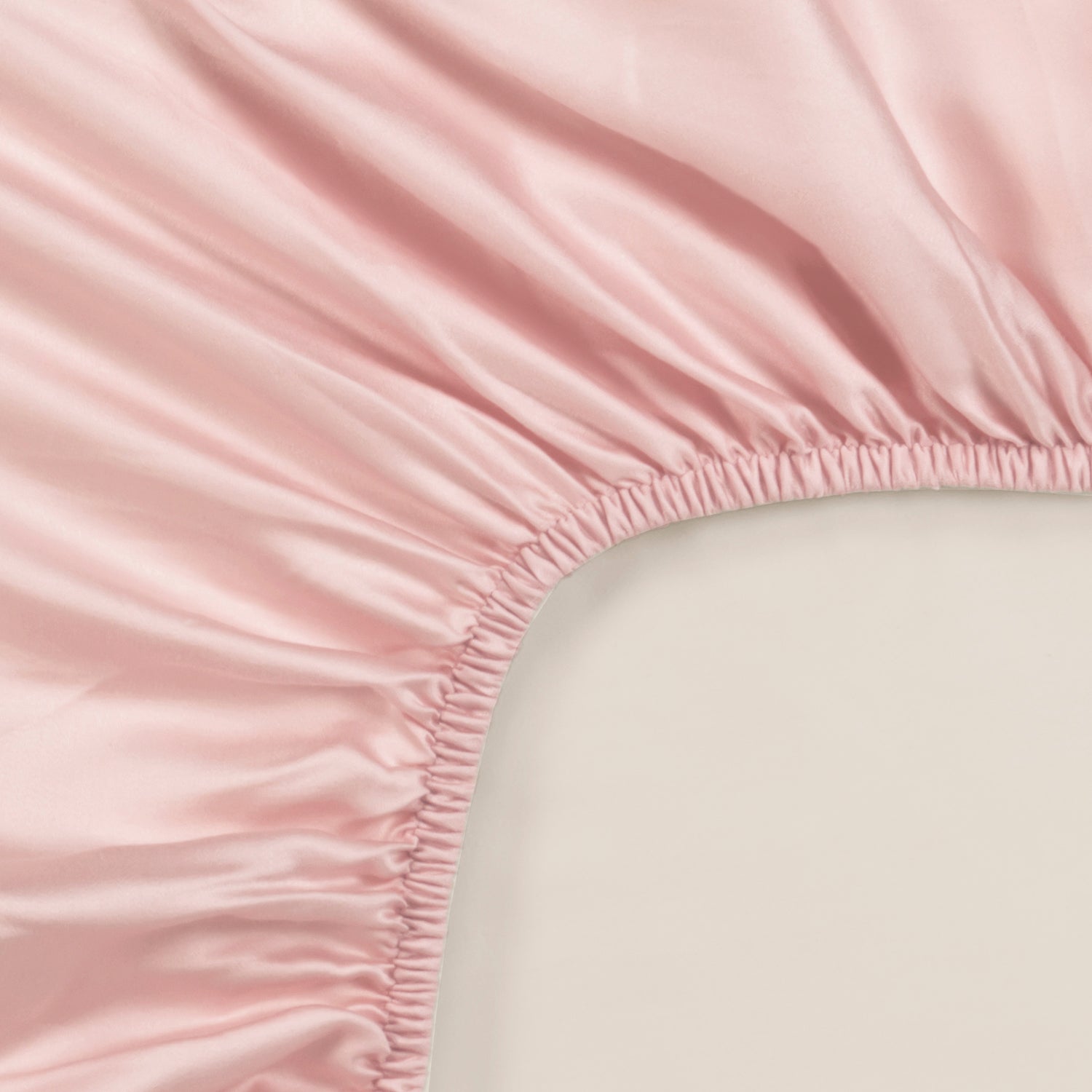 Soft pink Tencel™ sateen fitted sheet corner with elastic edge on beige background.