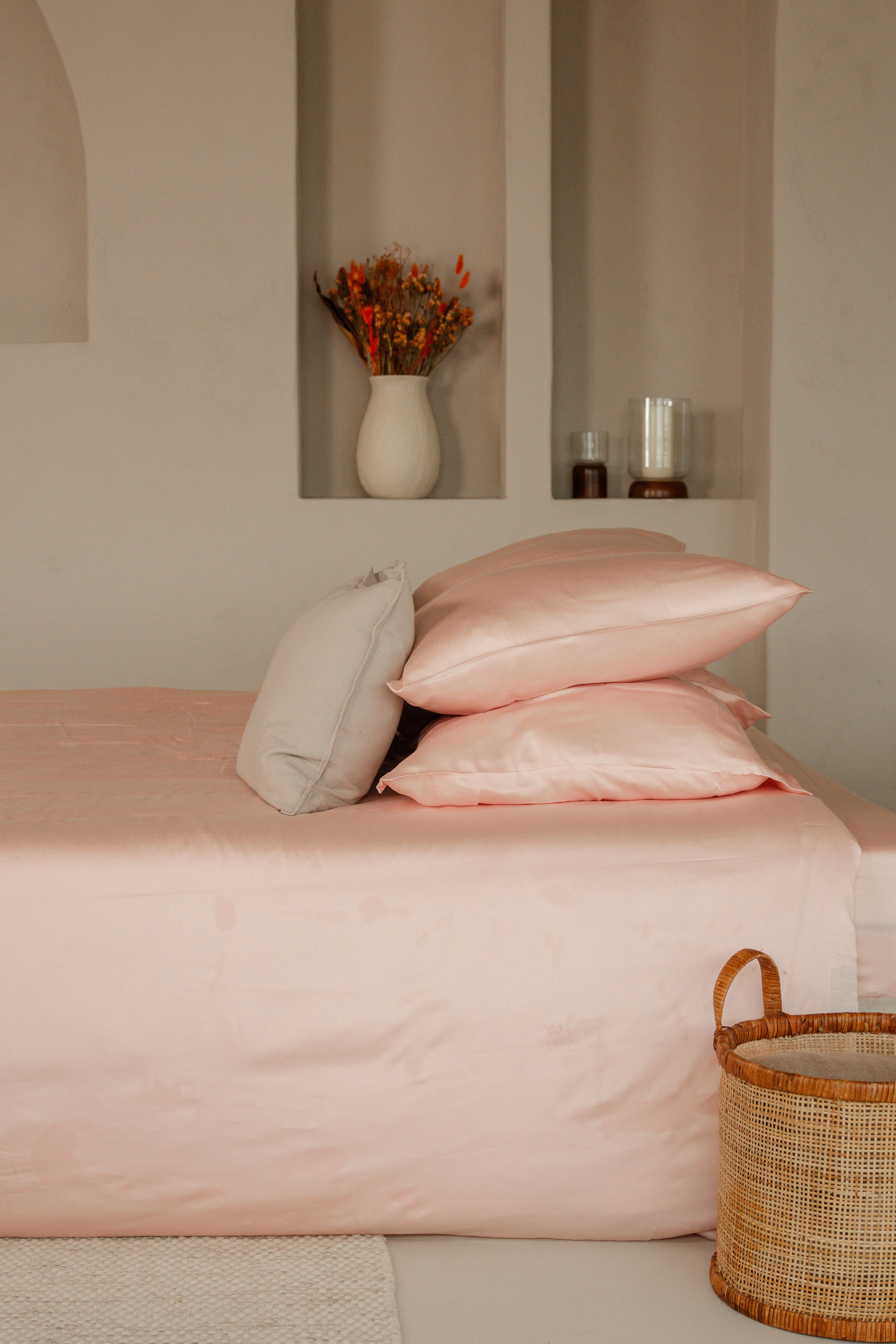 Soft blush pink Tencel sateen flat sheet with matching pillowcases on a bed with beige accent pillow and wicker basket nearby.